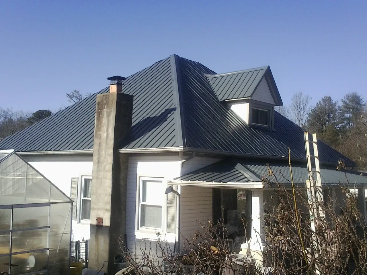 Dark blue standing seam metal roof on a white farmhouse with dormer — Slate & Tile Roof Repair by Roofing Brothers in Mcadoo