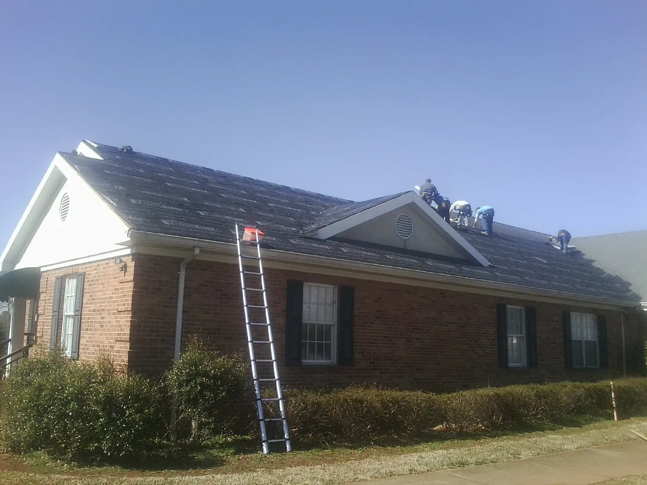 Crew tearing shingles off a brick ranch roof with a ladder set — Emergency Roof Repair work by our crew in Mcadoo