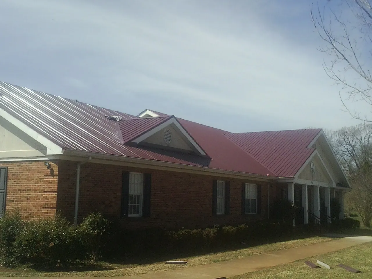 Red metal roof with gabled entries on a long brick building, from a Hail Damage Roof Repair job in Mcadoo