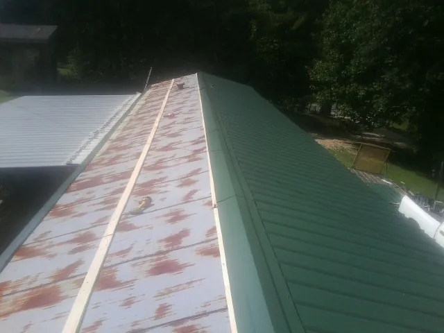 Old rusted panels beside newly installed green metal roofing — Wind Damage Roof Repair by Roofing Brothers in Mcadoo