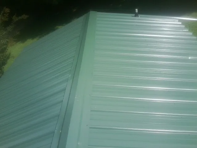 New green metal panels meeting at the ridge of a roof — Flat Roof Repair work by our crew in Mcadoo