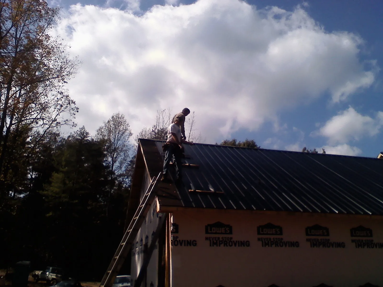 Roofer fastening dark metal panels high against a cloudy sky, from a Roof Inspection job in Mcadoo