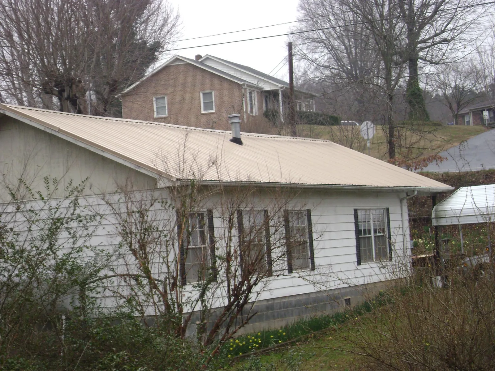 Tan metal roof on a white sided house set into a hillside — Commercial Roofing by Roofing Brothers in Mcadoo