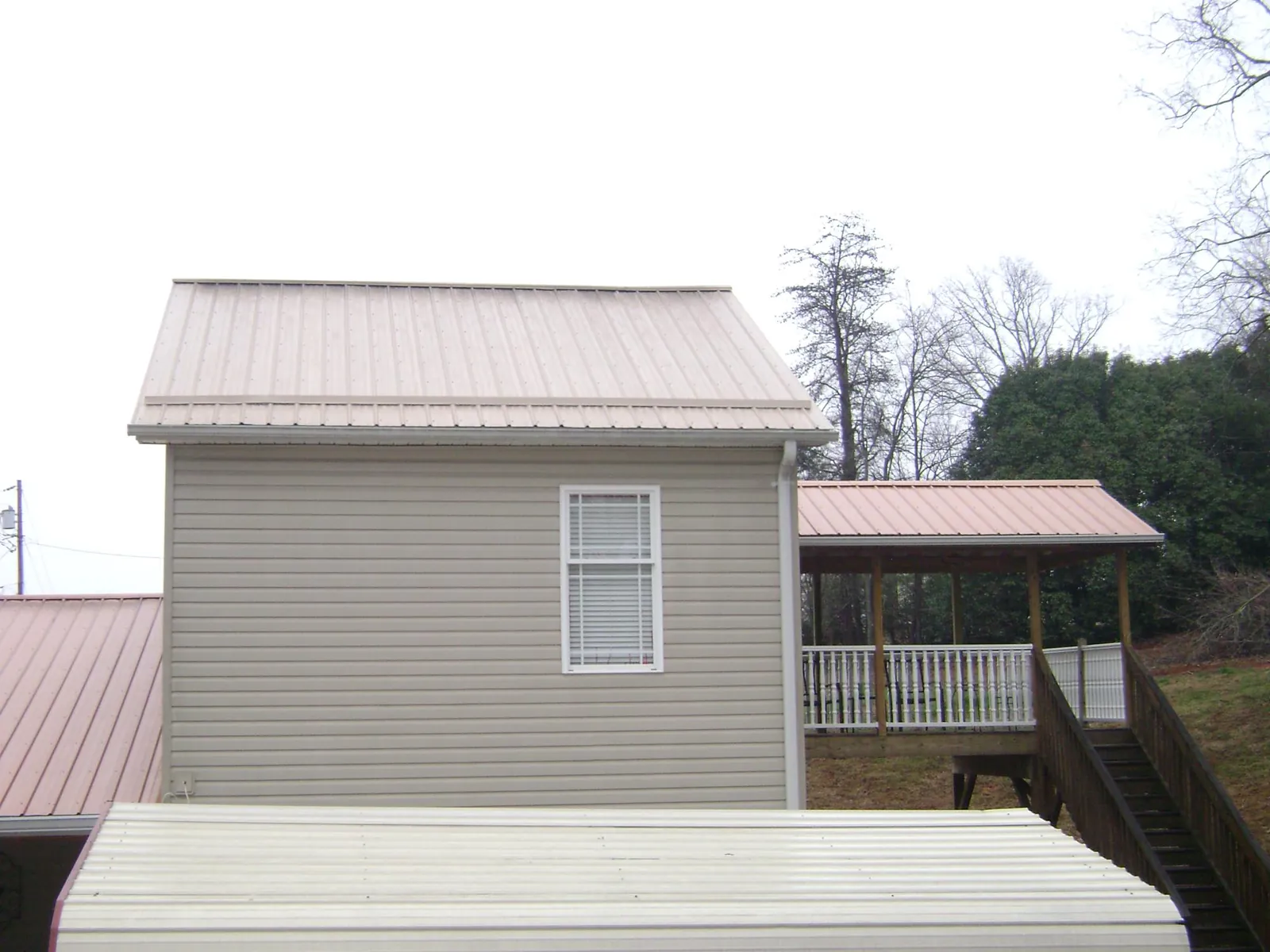 Tan metal roofs on a two story addition and attached porch, from a Roof Replacement job in Mcadoo